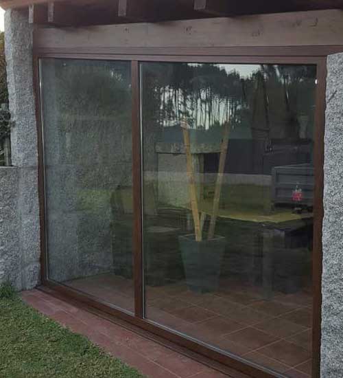 Fotografía de un gran ventanal de una casa, puerta corredera de cristal color nogal. Proyecto hecho por Top Ventana Reforma en colaboración con su red de profesionales de la construcción y reformas.